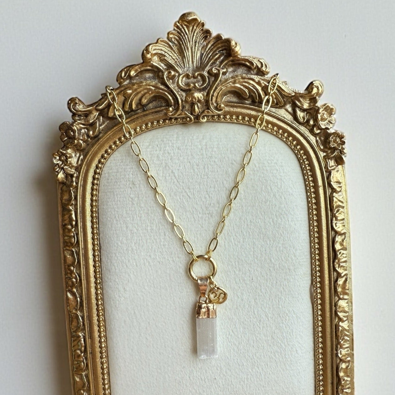 Gold necklace with a clear pendant in an ornate gold frame on a light gray background